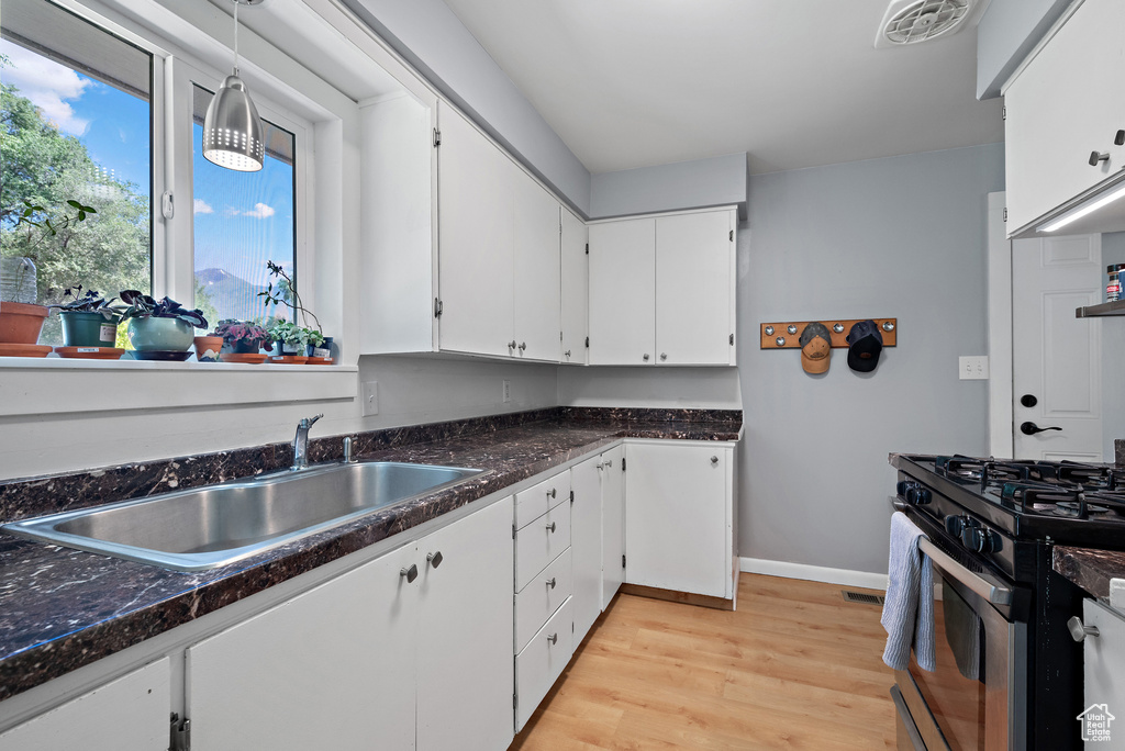 Kitchen featuring stainless steel gas stove, white cabinetry, light wood-style flooring, pendant lighting, and dark stone countertops