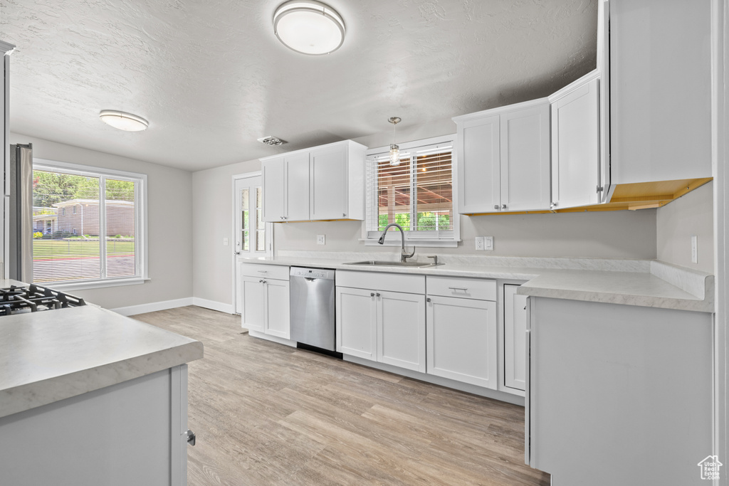 Kitchen featuring dishwasher, light wood finished floors, white cabinetry, light countertops, and a textured ceiling