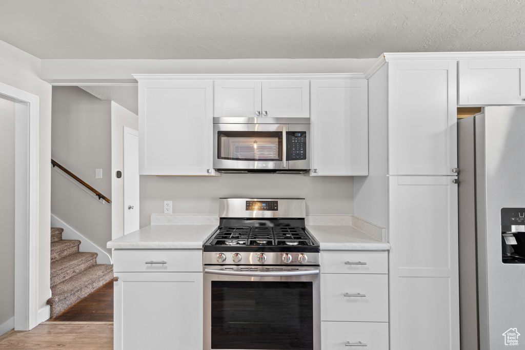 Kitchen with appliances with stainless steel finishes, wood finished floors, light countertops, and white cabinets