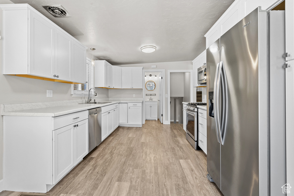 Kitchen with appliances with stainless steel finishes, light wood finished floors, light countertops, and white cabinets