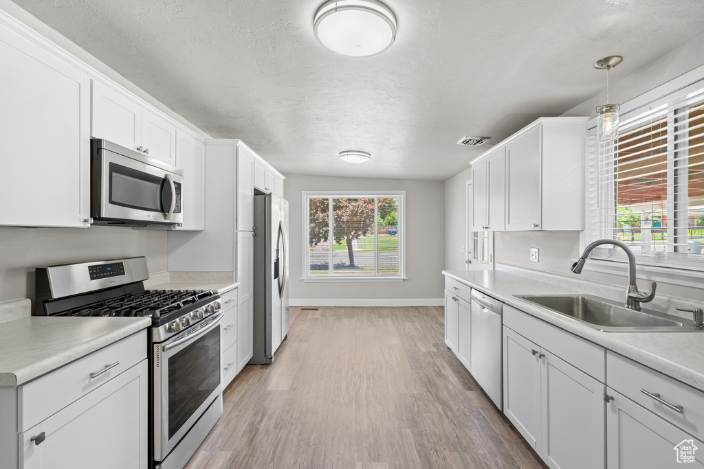 Kitchen with appliances with stainless steel finishes, light wood-style floors, white cabinets, plenty of natural light, and a textured ceiling