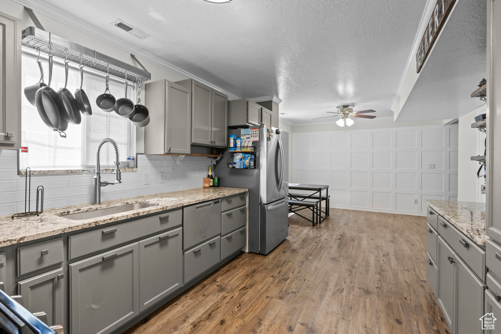 Kitchen featuring gray cabinetry, ceiling fan, freestanding refrigerator, wood finished floors, and light stone countertops