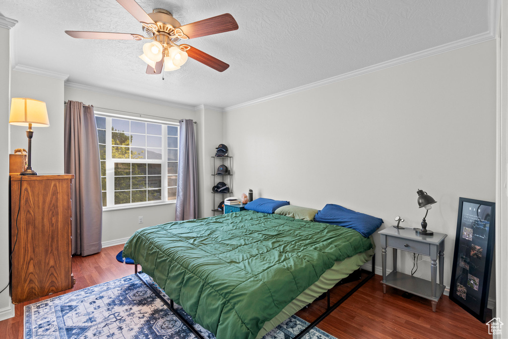 Bedroom featuring wood finished floors, a textured ceiling, crown molding, and a ceiling fan