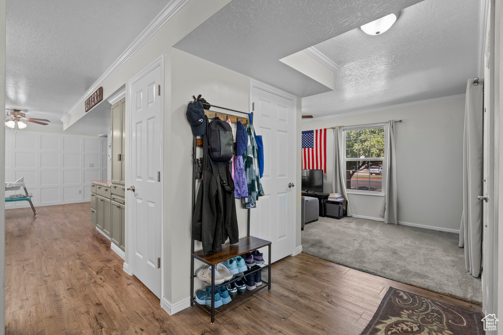 Hall featuring a textured ceiling, wood finished floors, and crown molding