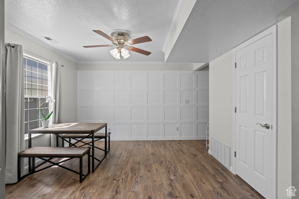 Dining area with a ceiling fan, a textured ceiling, dark wood-type flooring, and ornamental molding