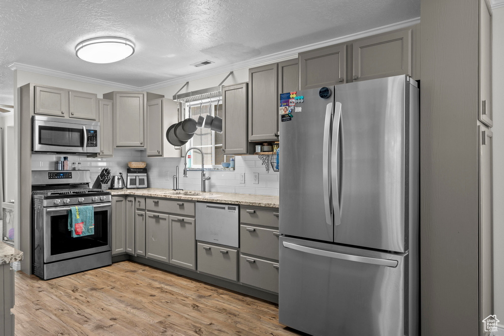 Kitchen with stainless steel appliances, gray cabinetry, tasteful backsplash, a textured ceiling, and ornamental molding