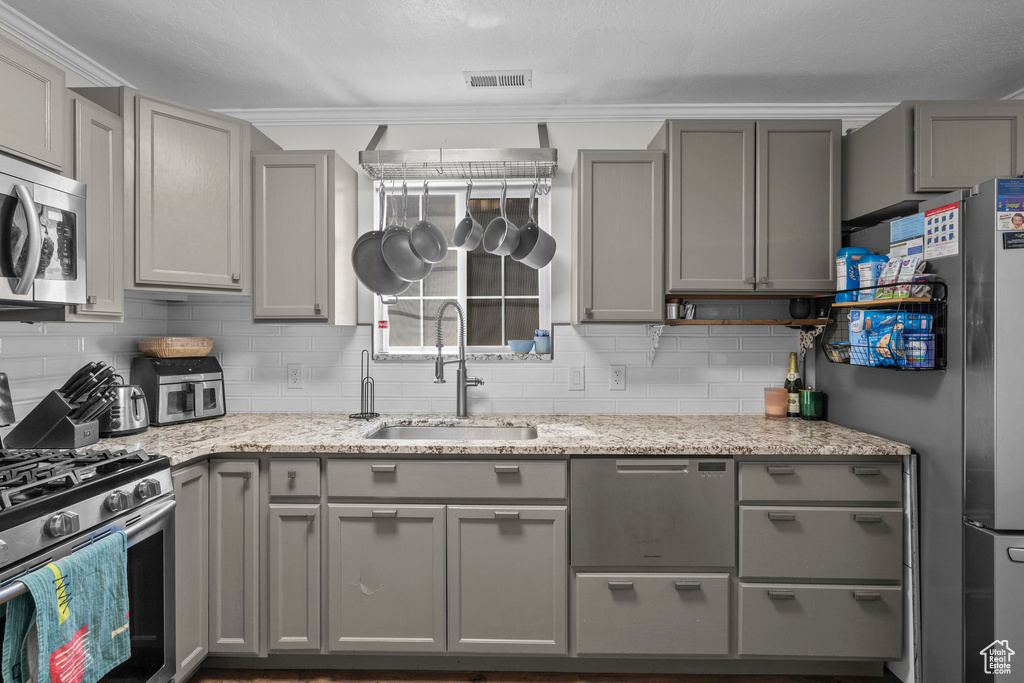 Kitchen featuring gray cabinets, appliances with stainless steel finishes, decorative backsplash, and light stone countertops