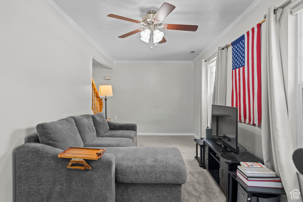 Living area featuring carpet, crown molding, a ceiling fan, and stairway