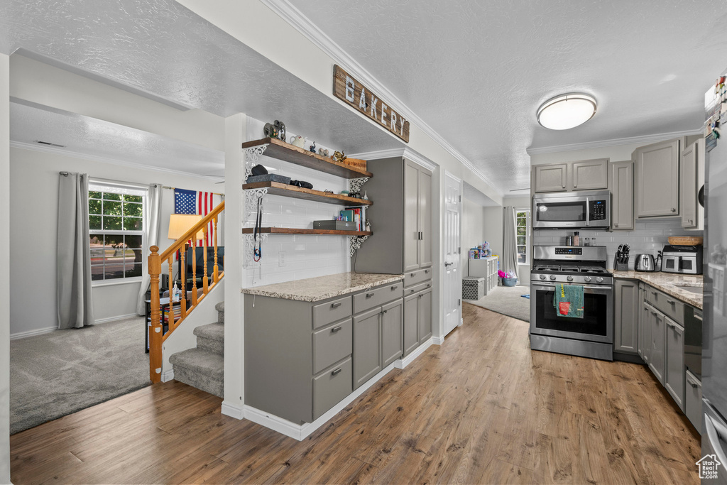 Kitchen featuring gray cabinets, stainless steel appliances, ornamental molding, wood finished floors, and light stone countertops