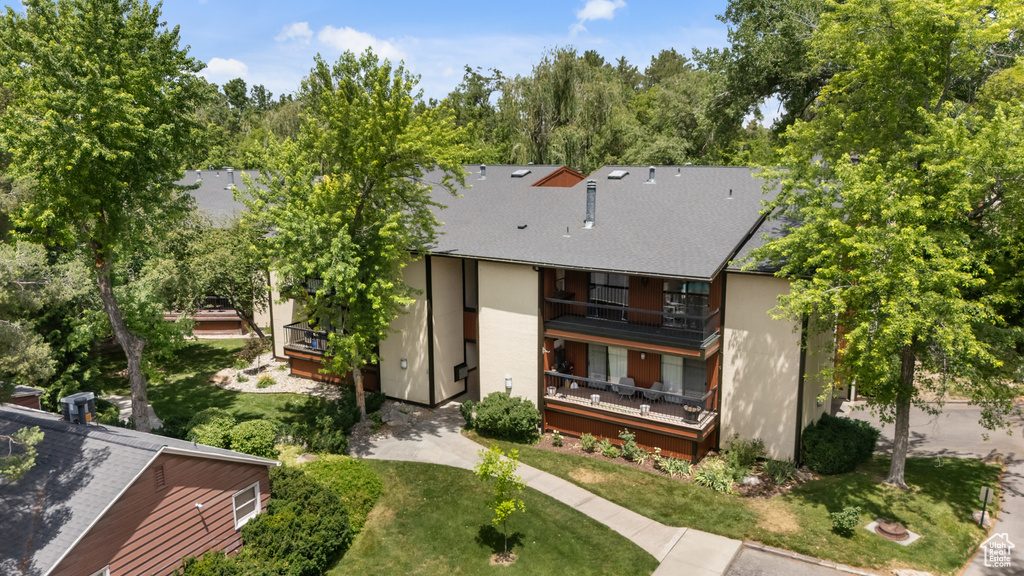 Back of house featuring a balcony, stucco siding, roof with shingles, and a yard