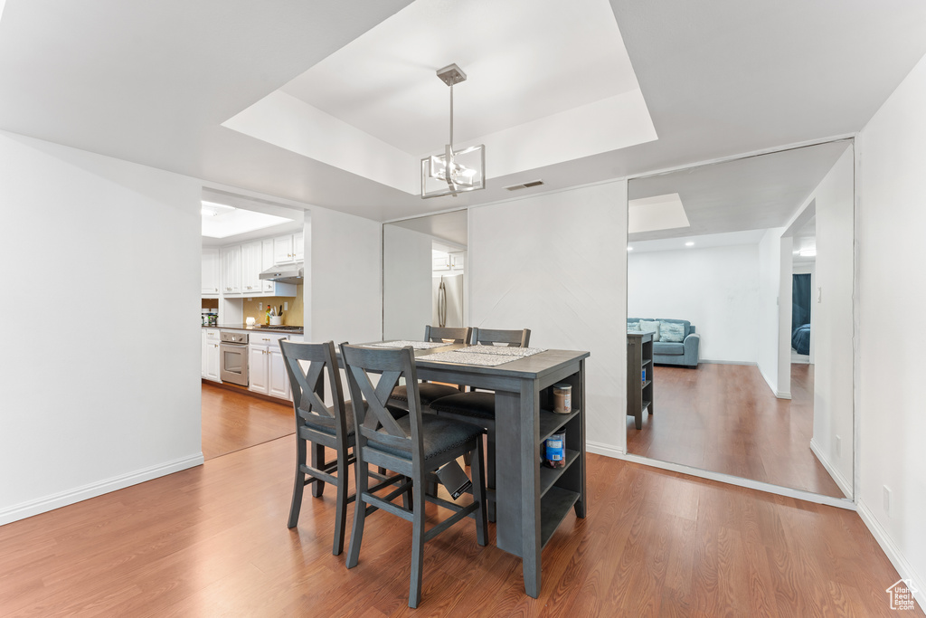 Dining area with a tray ceiling, a chandelier, and light wood-type flooring