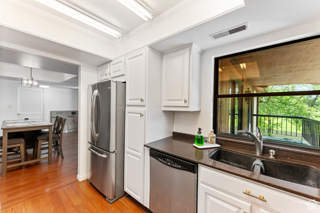Kitchen with stainless steel appliances, light wood-style flooring, white cabinetry, and dark stone counters