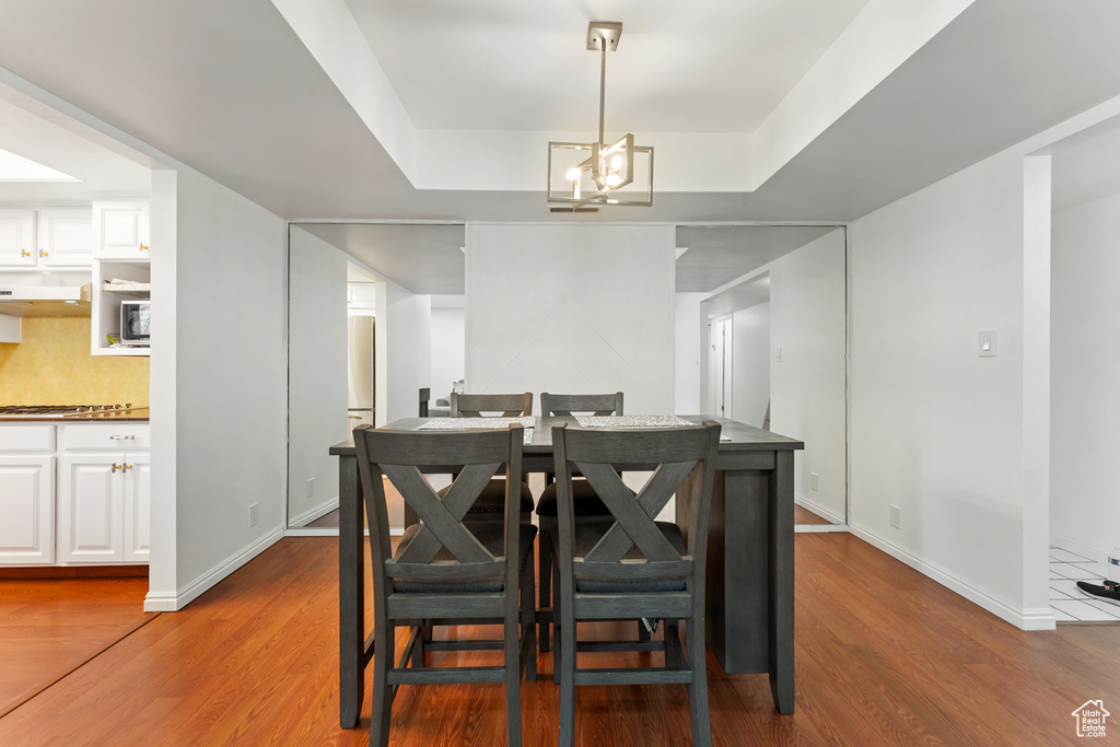 Dining area with wood finished floors, a raised ceiling, and a chandelier