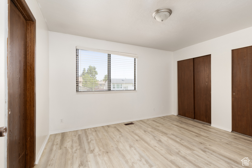 Unfurnished bedroom with light wood finished floors and multiple closets