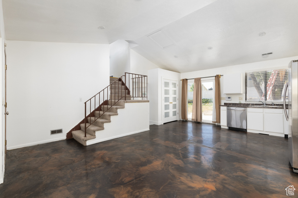 Unfurnished living room featuring lofted ceiling and stairs