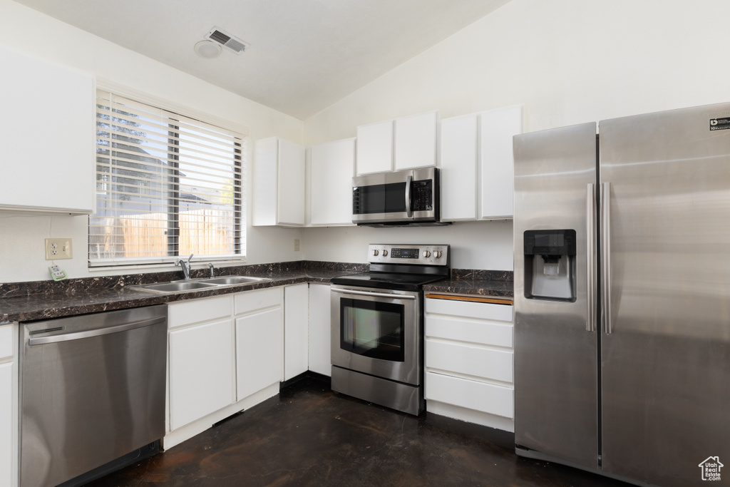 Kitchen featuring stainless steel appliances, lofted ceiling, white cabinets, and concrete flooring