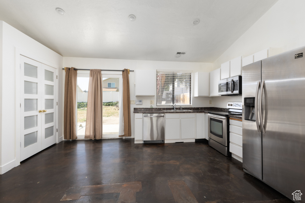Kitchen with stainless steel appliances, dark countertops, plenty of natural light, and white cabinetry
