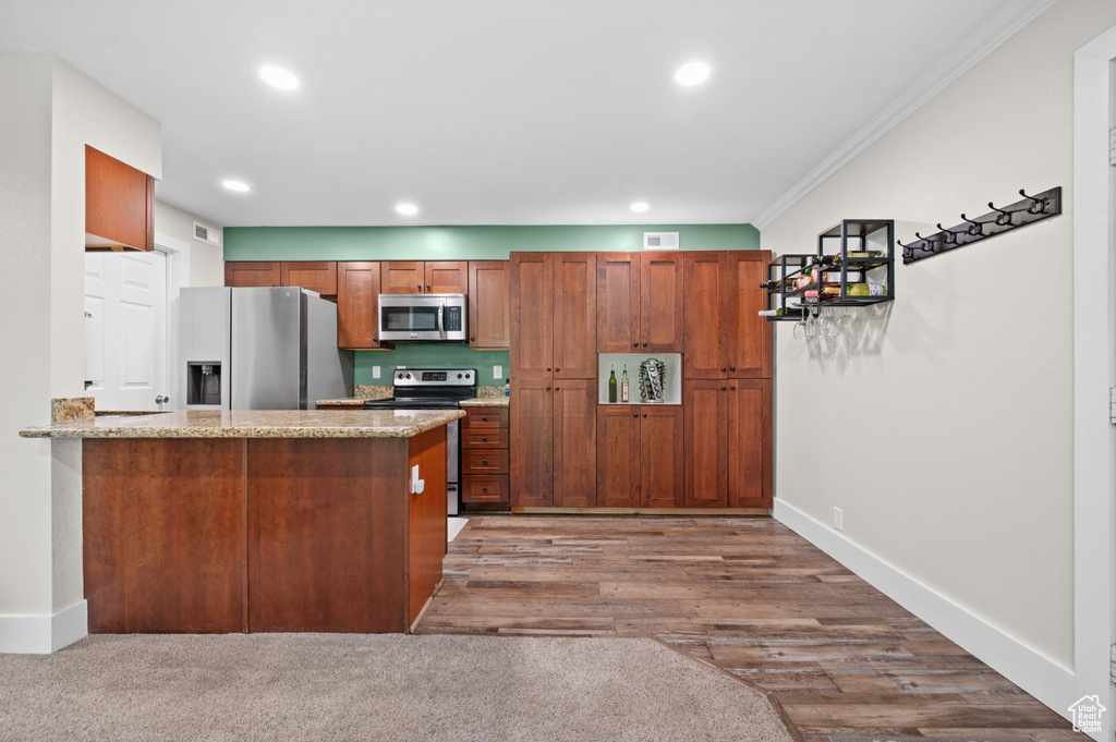 Kitchen featuring appliances with stainless steel finishes, ornamental molding, recessed lighting, brown cabinets, and a peninsula