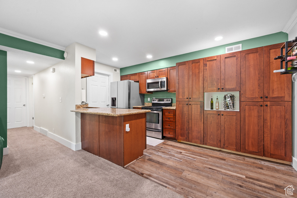 Kitchen with stainless steel appliances, a peninsula, recessed lighting, brown cabinetry, and light stone counters