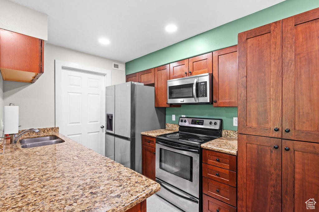 Kitchen featuring stainless steel appliances, light stone counters, brown cabinets, and recessed lighting