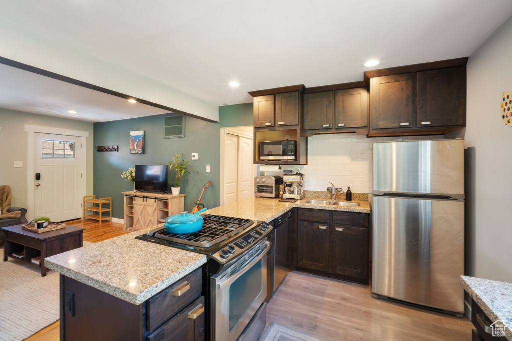 Kitchen with appliances with stainless steel finishes, light wood finished floors, decorative backsplash, dark brown cabinets, and light stone countertops
