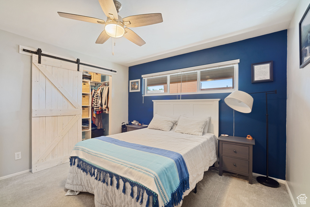 Carpeted bedroom featuring a barn door, a walk in closet, a closet, and ceiling fan
