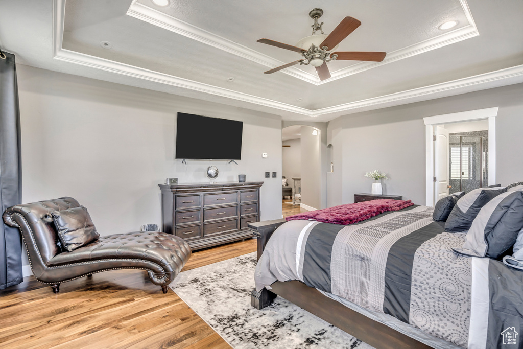 Bedroom with a raised ceiling, crown molding, wood finished floors, arched walkways, and recessed lighting