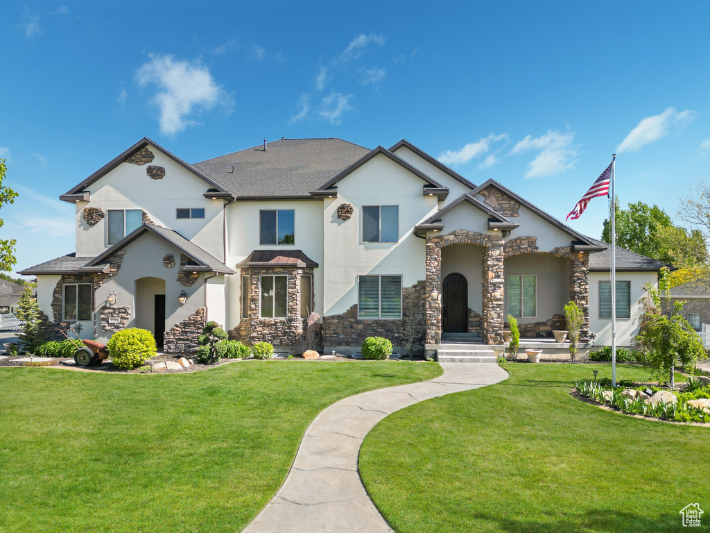 View of front facade featuring stucco siding, stone siding, and a front yard