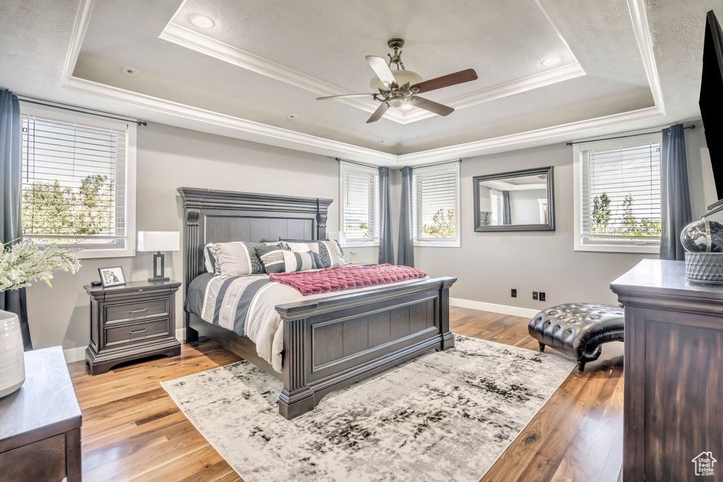 Bedroom featuring a raised ceiling, multiple windows, crown molding, light wood-style floors, and recessed lighting