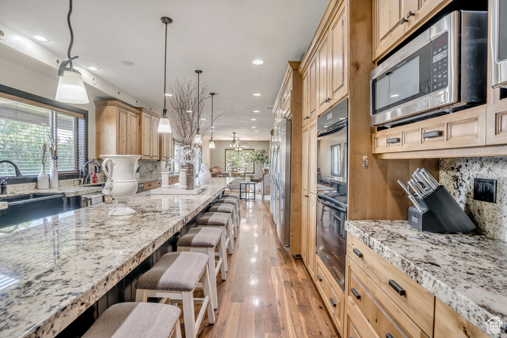 Kitchen with appliances with stainless steel finishes, a breakfast bar area, recessed lighting, light wood-style floors, and backsplash