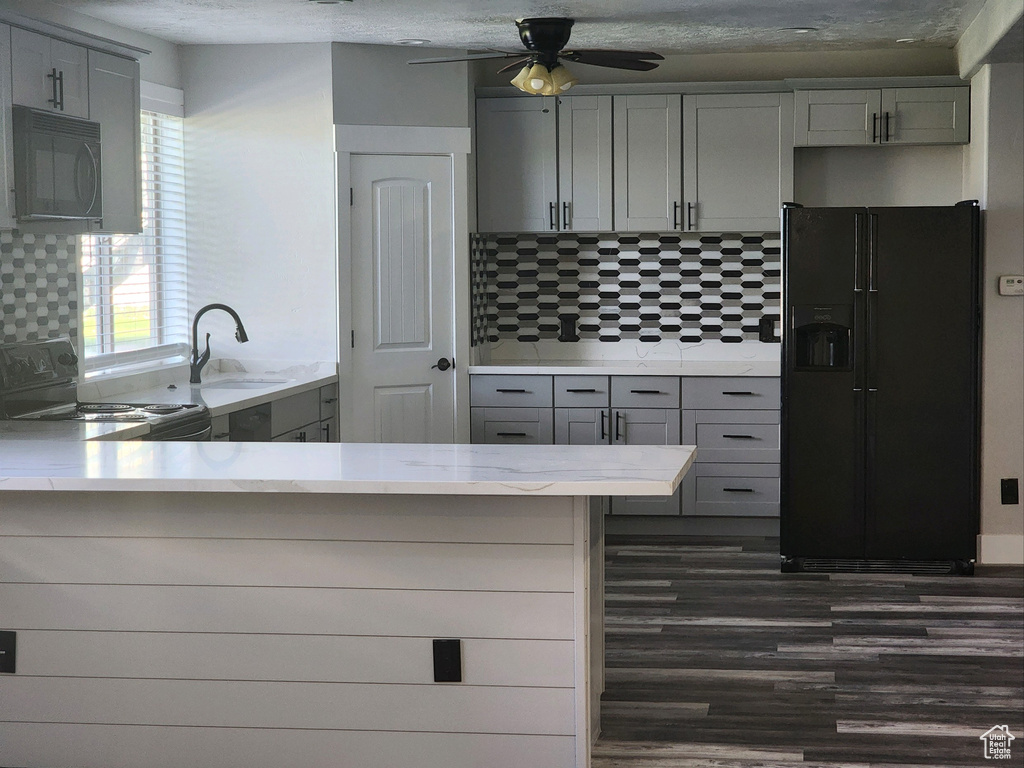 Kitchen with black appliances, gray cabinetry, dark wood-type flooring, and tasteful backsplash