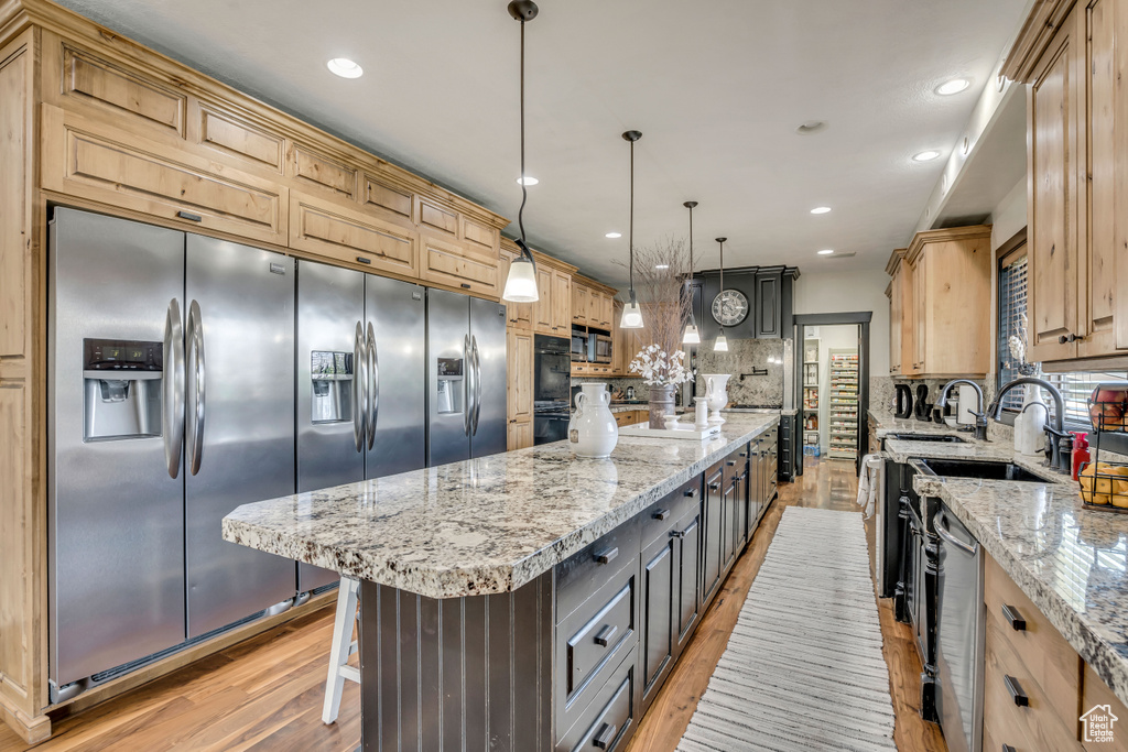 Kitchen with light wood-style flooring, a large island, backsplash, light stone countertops, and stainless steel appliances