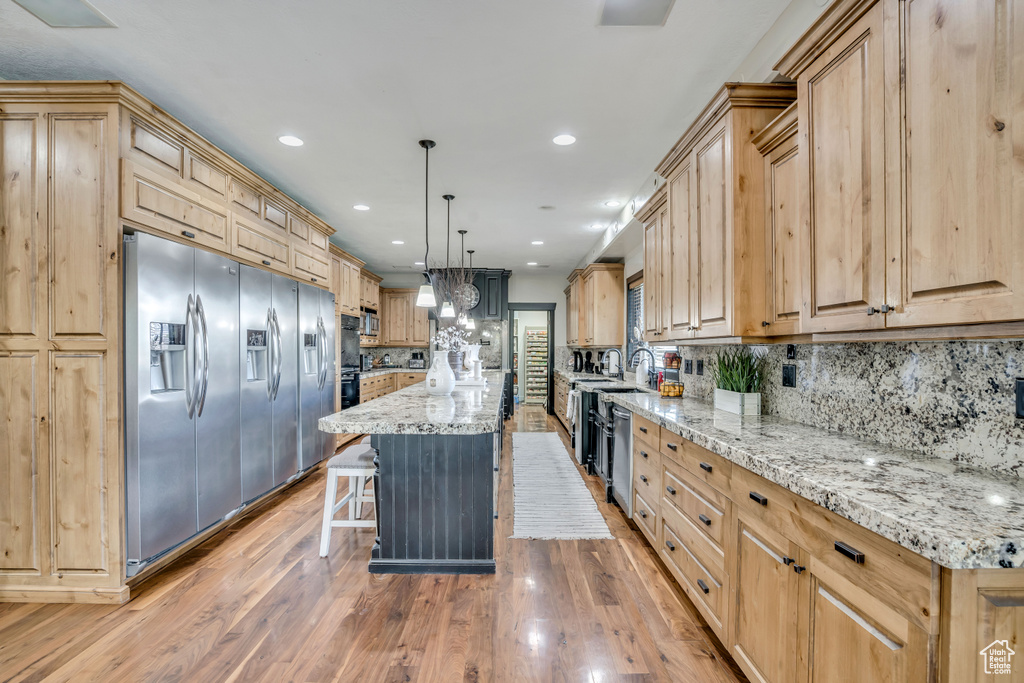Kitchen featuring stainless steel appliances, light brown cabinetry, light stone countertops, a breakfast bar area, and a center island