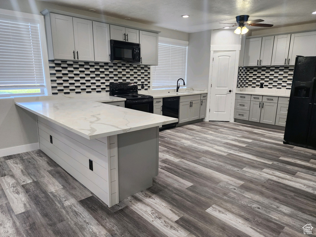 Kitchen featuring black appliances, a peninsula, tasteful backsplash, wood finished floors, and a ceiling fan