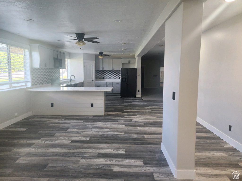 Kitchen featuring black fridge, light countertops, a peninsula, ceiling fan, and dark wood-type flooring