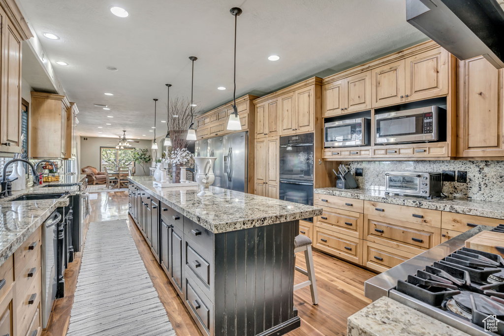 Kitchen with appliances with stainless steel finishes, light brown cabinetry, a large island, recessed lighting, and a breakfast bar