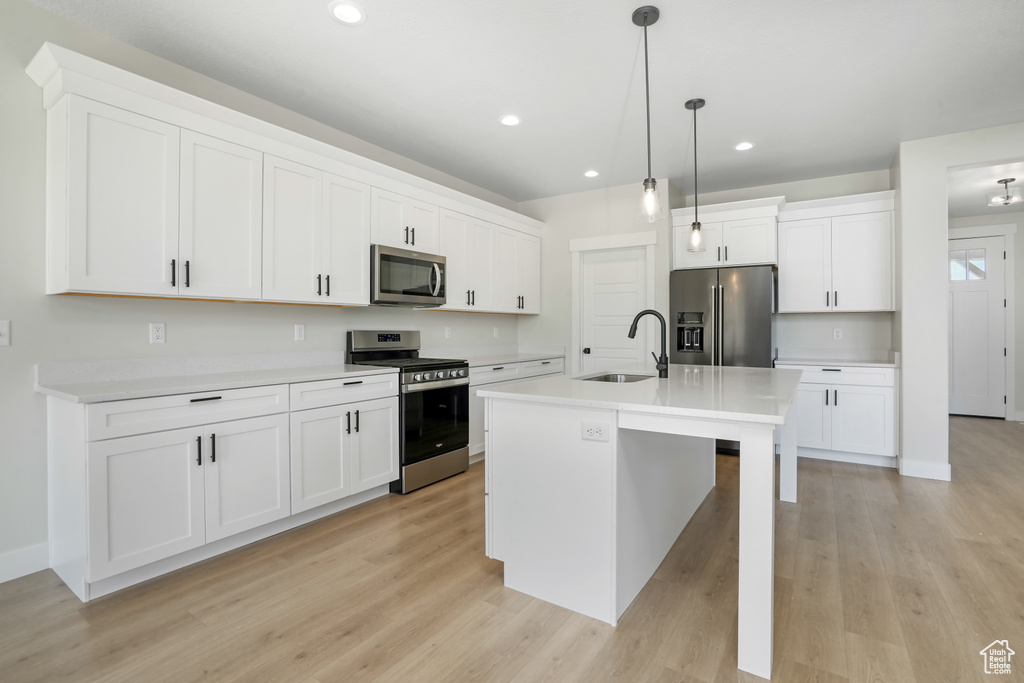 Kitchen with appliances with stainless steel finishes, light wood-style flooring, a center island with sink, recessed lighting, and white cabinets