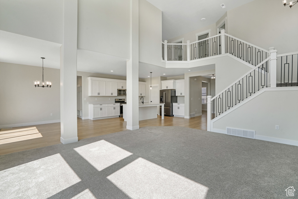 Unfurnished living room featuring light colored carpet, a chandelier, a high ceiling, and stairway