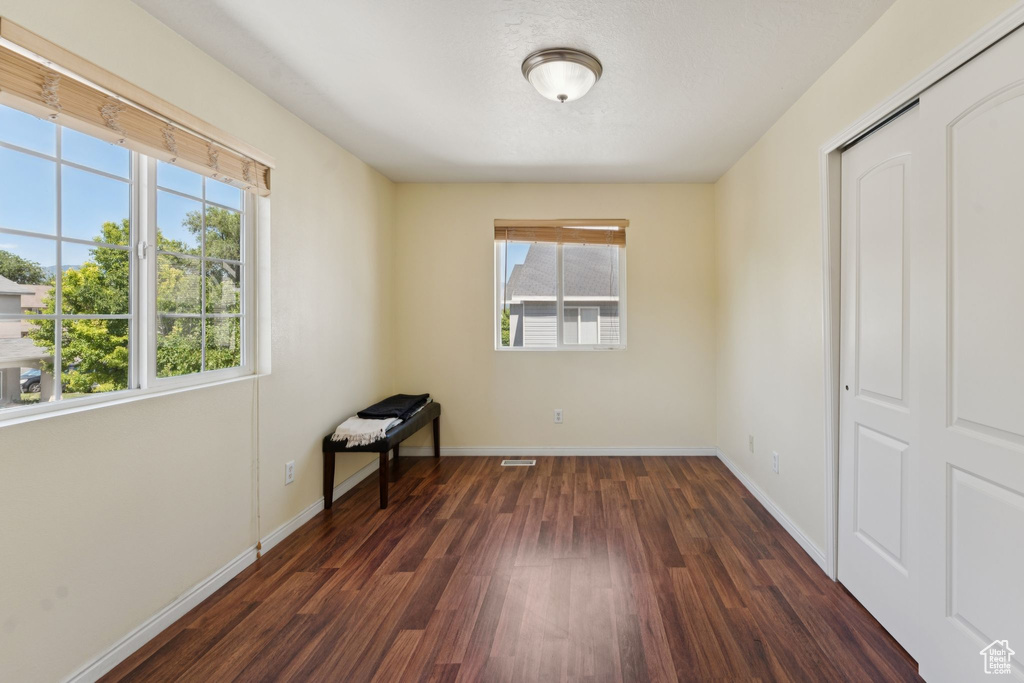 Unfurnished bedroom with multiple windows, dark wood-type flooring, and a closet