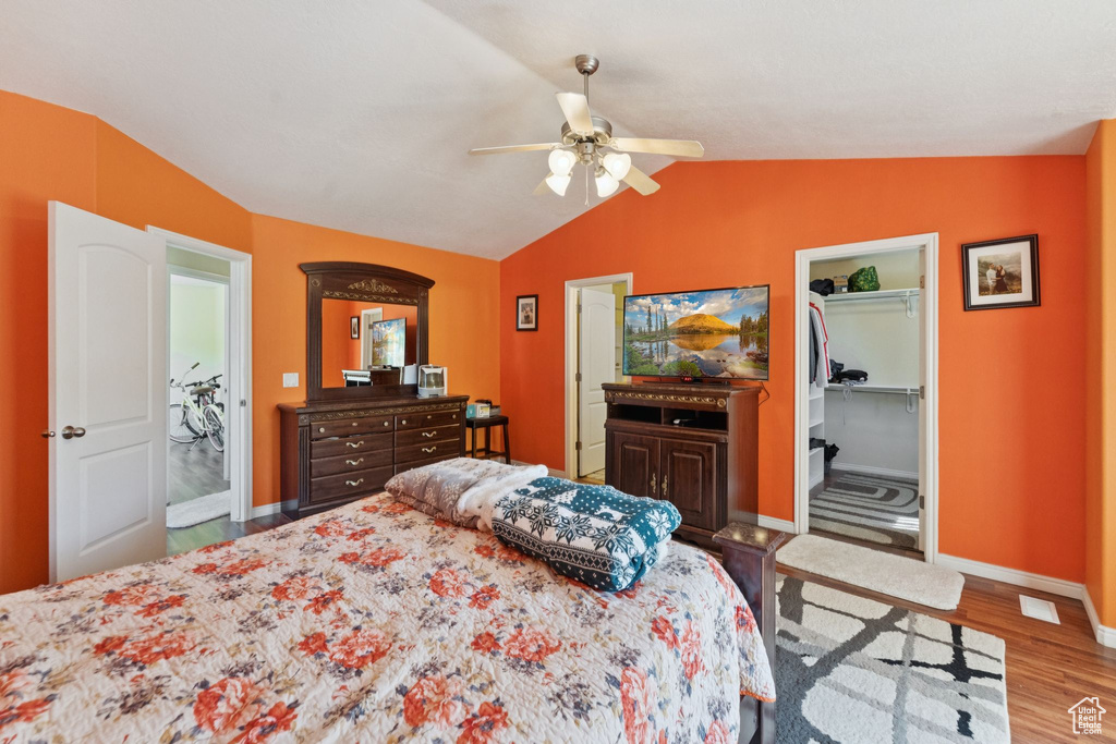 Bedroom featuring wood finished floors, lofted ceiling, ceiling fan, and a walk in closet