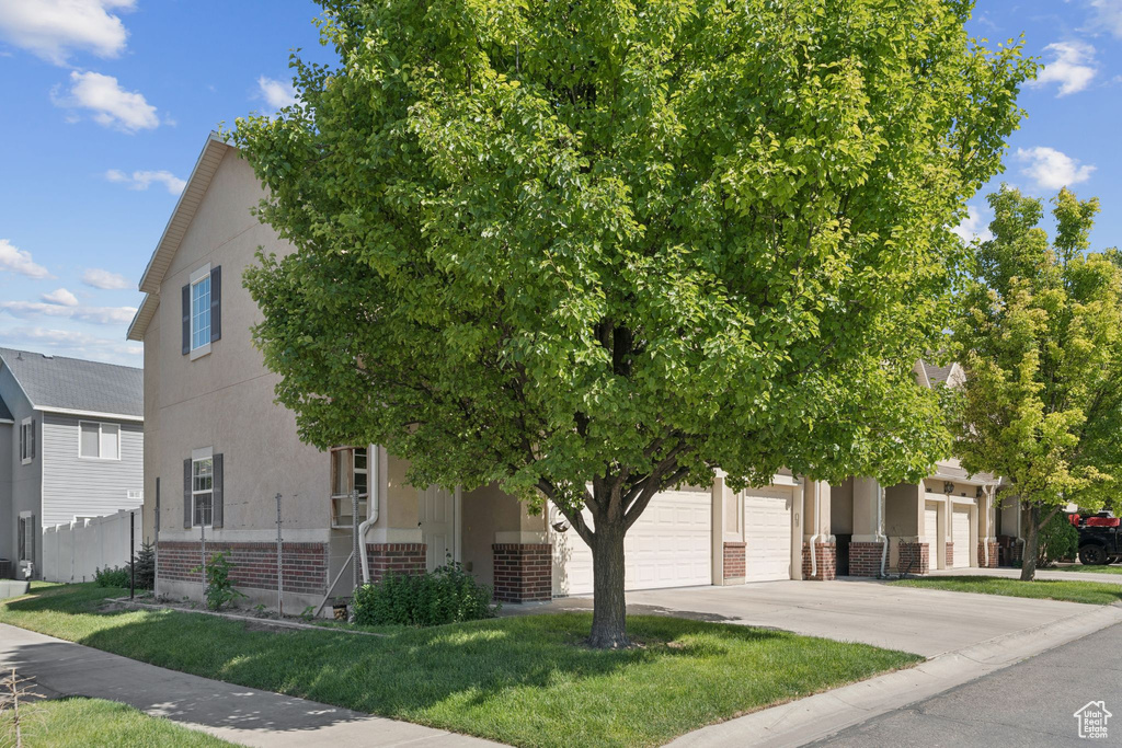View of property hidden behind natural elements featuring brick siding, driveway, and stucco siding