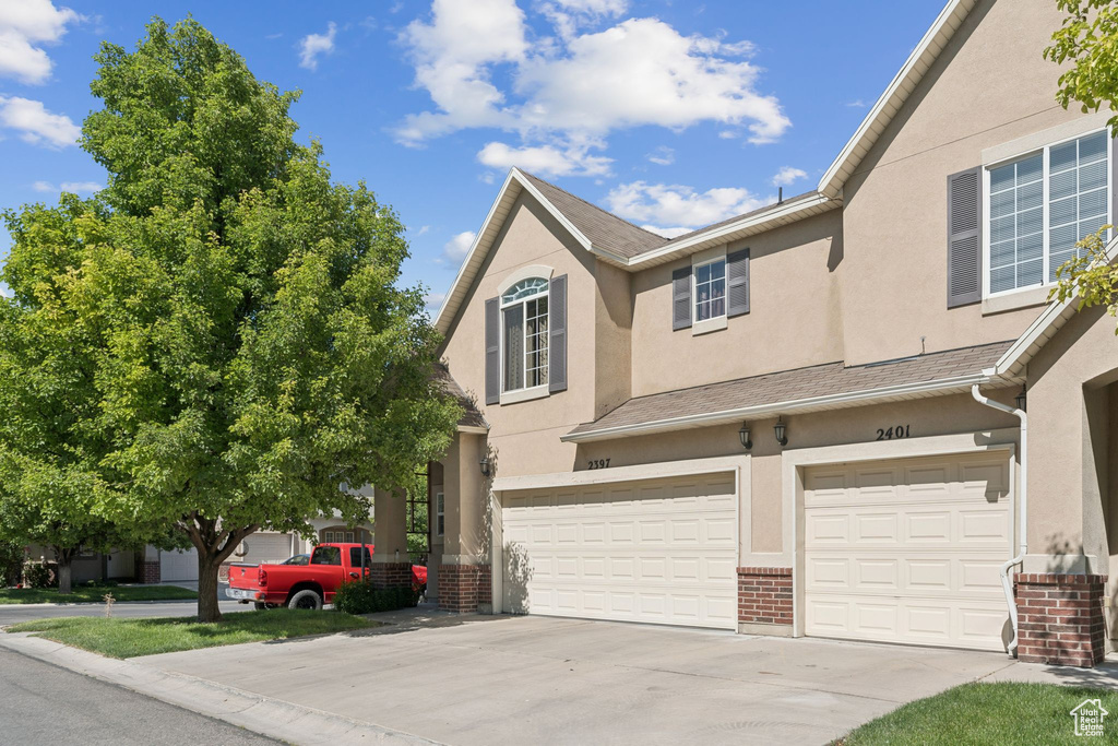 View of front of home featuring an attached garage, brick siding, driveway, and stucco siding