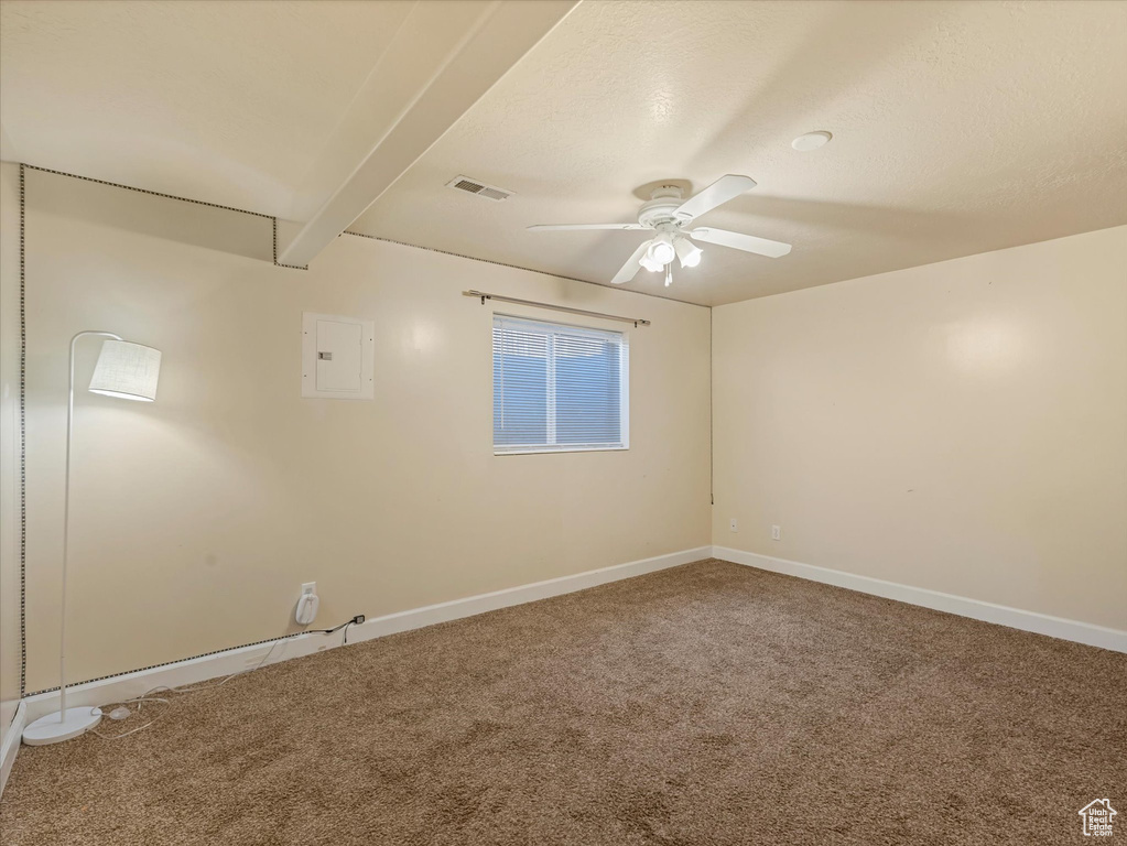 Carpeted empty room featuring a ceiling fan, electric panel, and beamed ceiling
