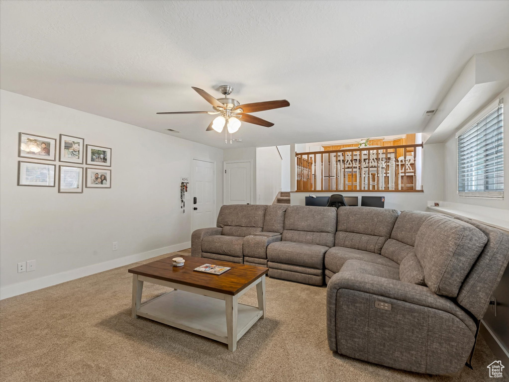 Carpeted living room featuring ceiling fan and baseboards