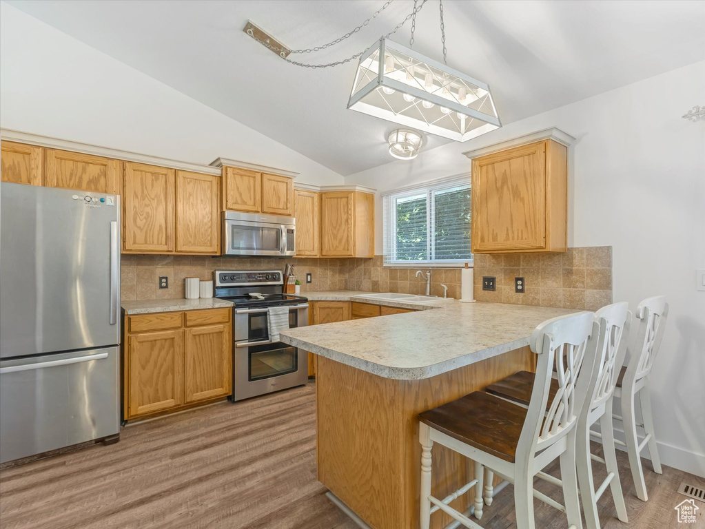 Kitchen with appliances with stainless steel finishes, light countertops, vaulted ceiling, a peninsula, and tasteful backsplash