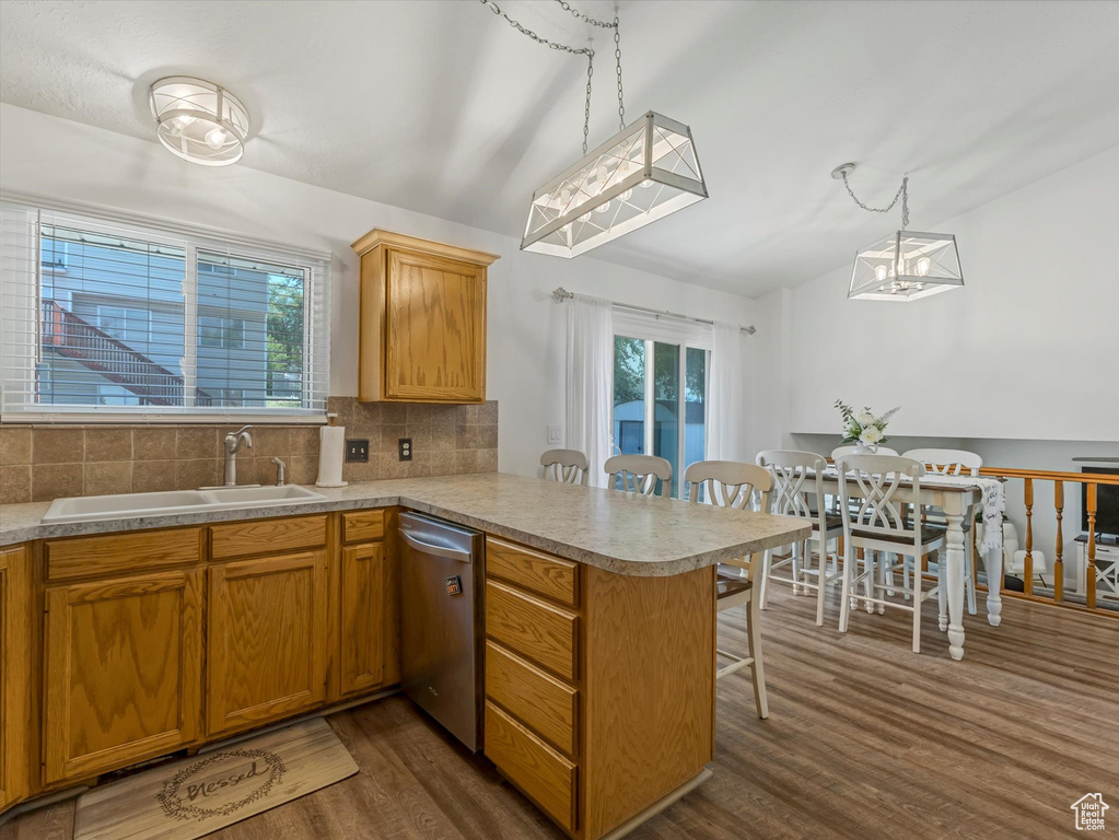 Kitchen featuring stainless steel dishwasher, a peninsula, dark wood-style flooring, a breakfast bar area, and tasteful backsplash