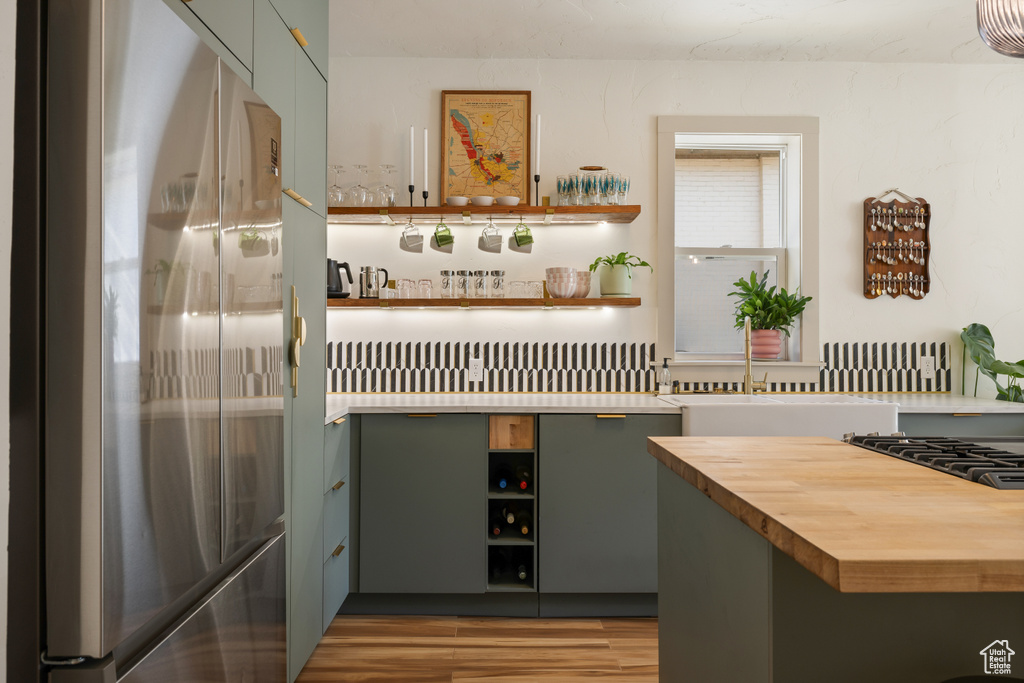 Kitchen view of stainless steel fridge, open shelves, wood counters, light wood-style flooring, and bar