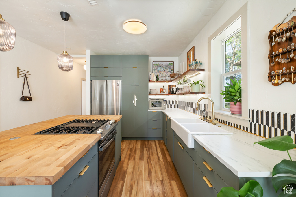 Kitchen with stainless steel appliances, wooden counters, light wood-style floors, open shelves, and pendant lighting