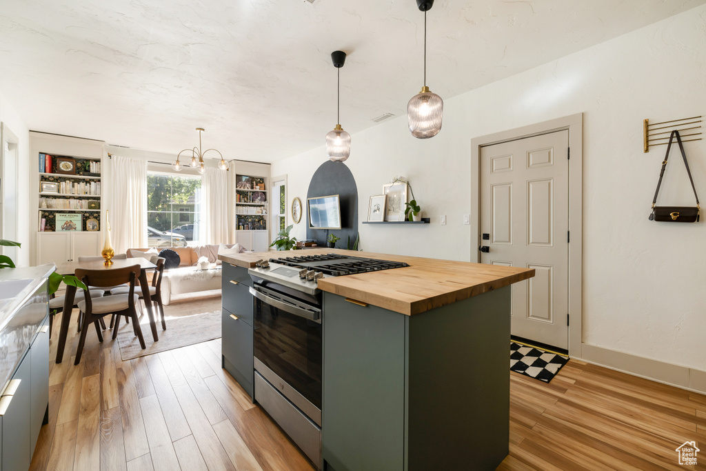Kitchen featuring stainless steel range with gas stovetop, butcher block counters, light wood finished floors, a center island, and hanging light fixtures