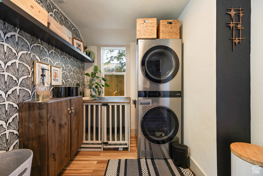 Washroom with stacked washing machine and dryer and light wood-style flooring